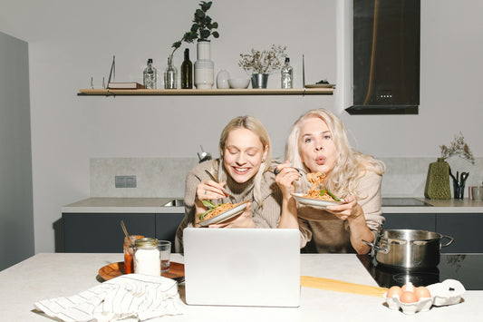 Two women of various ages eating happily at the kitchen counter, symbolizing healthy eating choices.