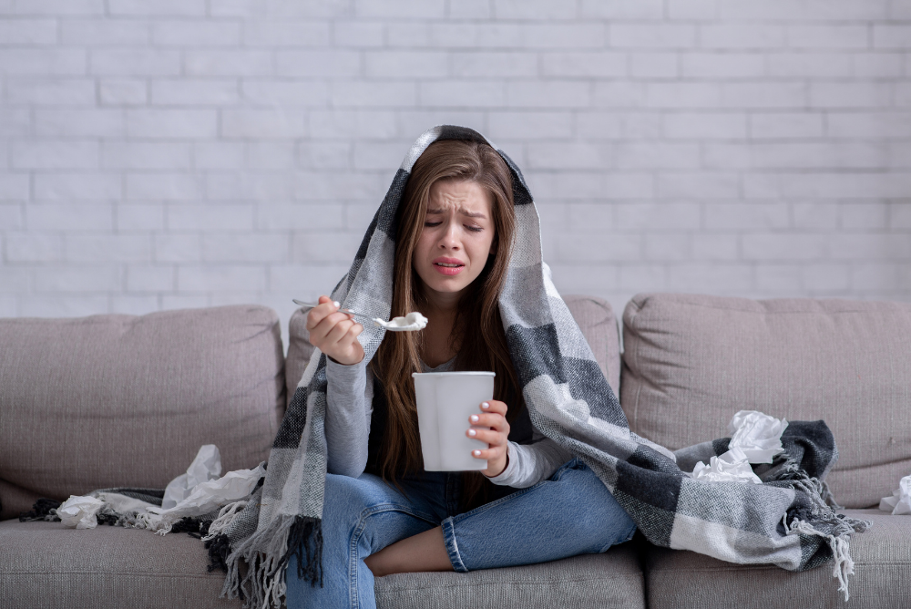 Woman sitting on a couch, eating ice cream and looking guilty.