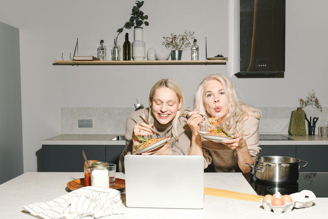 Two women of various ages eating happily at the kitchen counter, symbolizing healthy eating choices.