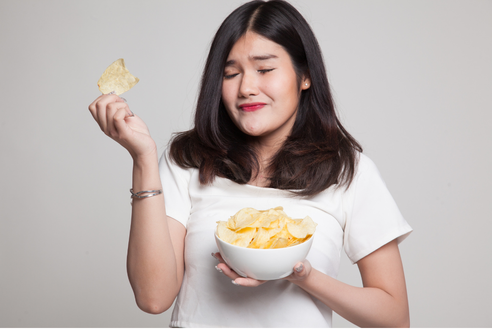 Woman eating chips in plain gray background.